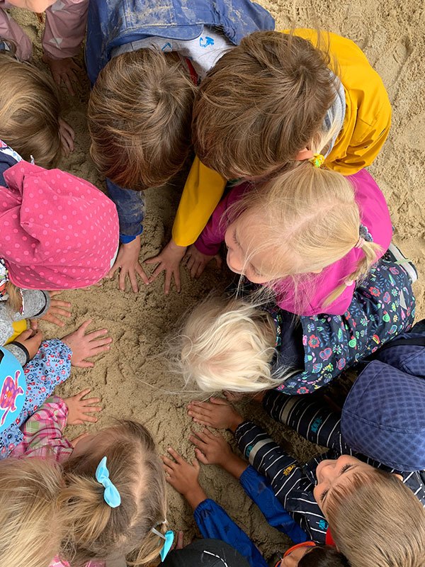 Kinder_01 Mehrere Kinder sitzen im Kreis im Sand und legen ihre Hände in die Mitte